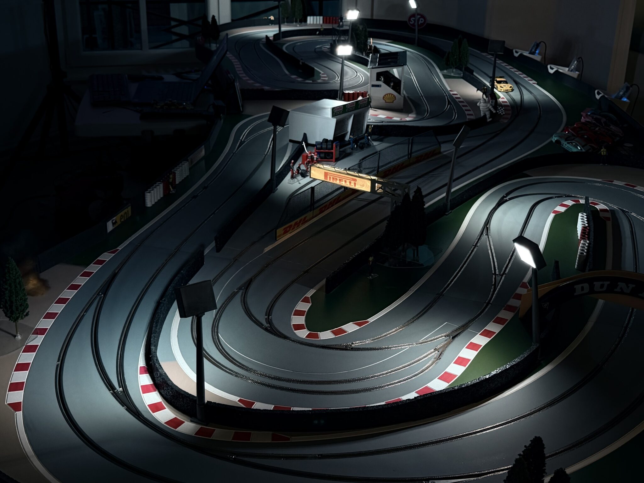 Vue plongeante sur le circuit miniature électrique Good Time Racing, avec virage en épingle, bordures rouge et blanc et éclairage de nuit