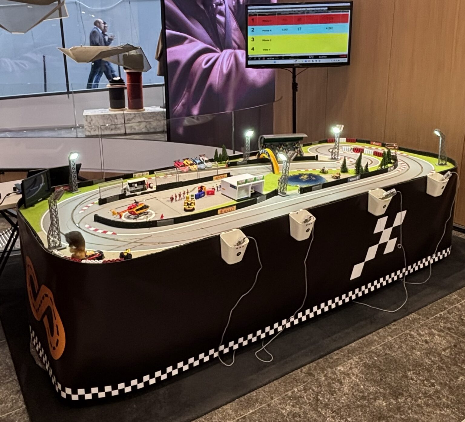 Le petit circuit installé dans un hall, avec habillage noir et damier, 4 supports de manettes et écran de classement